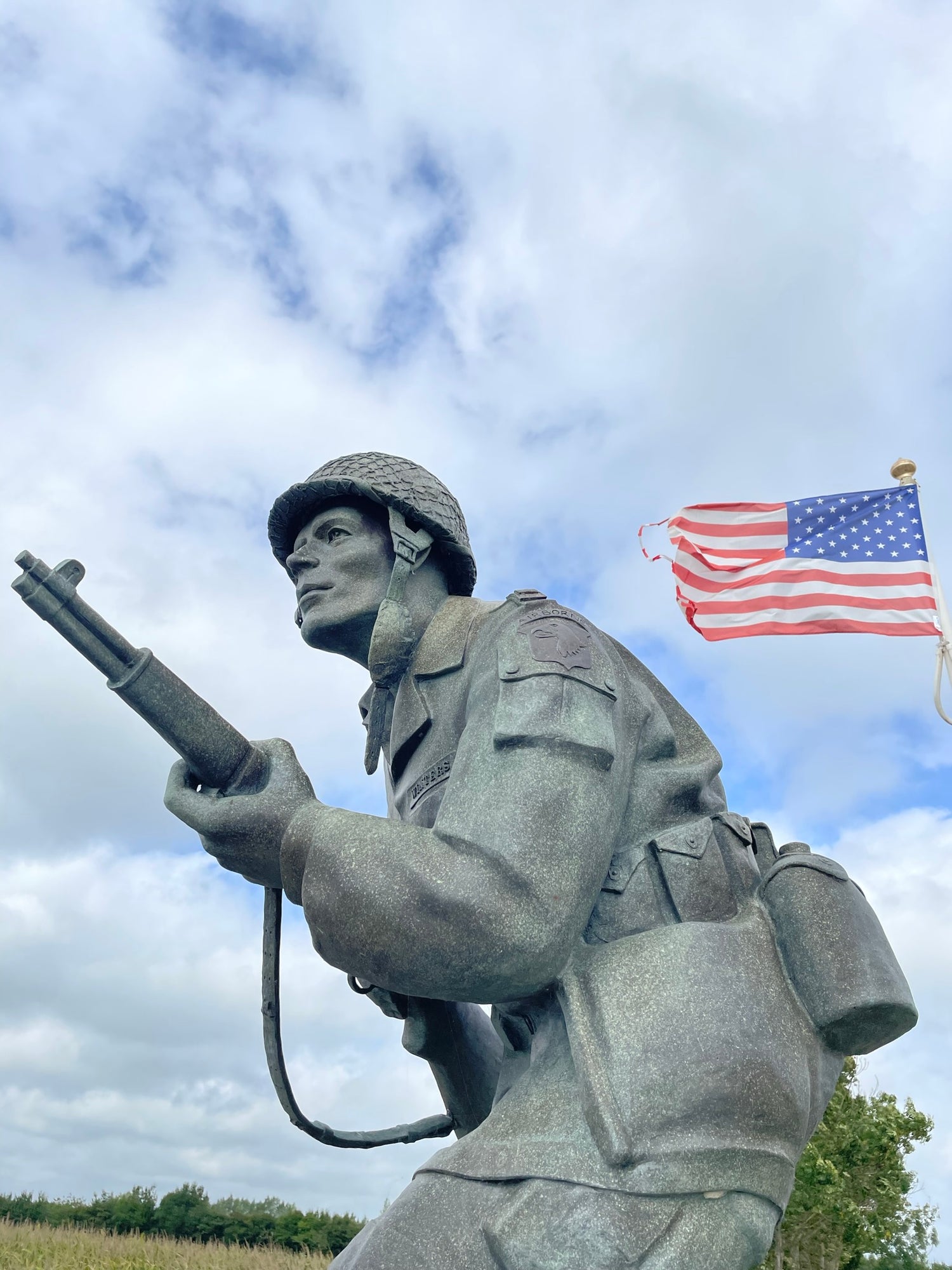 Statue of a soldier holding a rifle and an American flag against a cloudy sky. Dick Winters Leadership Memorial.