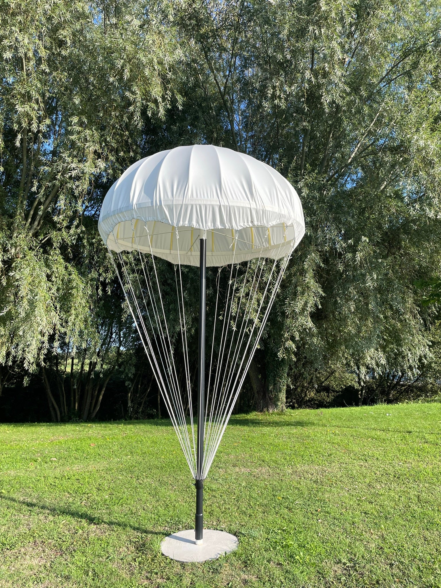White parachute canopy with ropes on a grassy area with trees in the background, outside of Carentan.