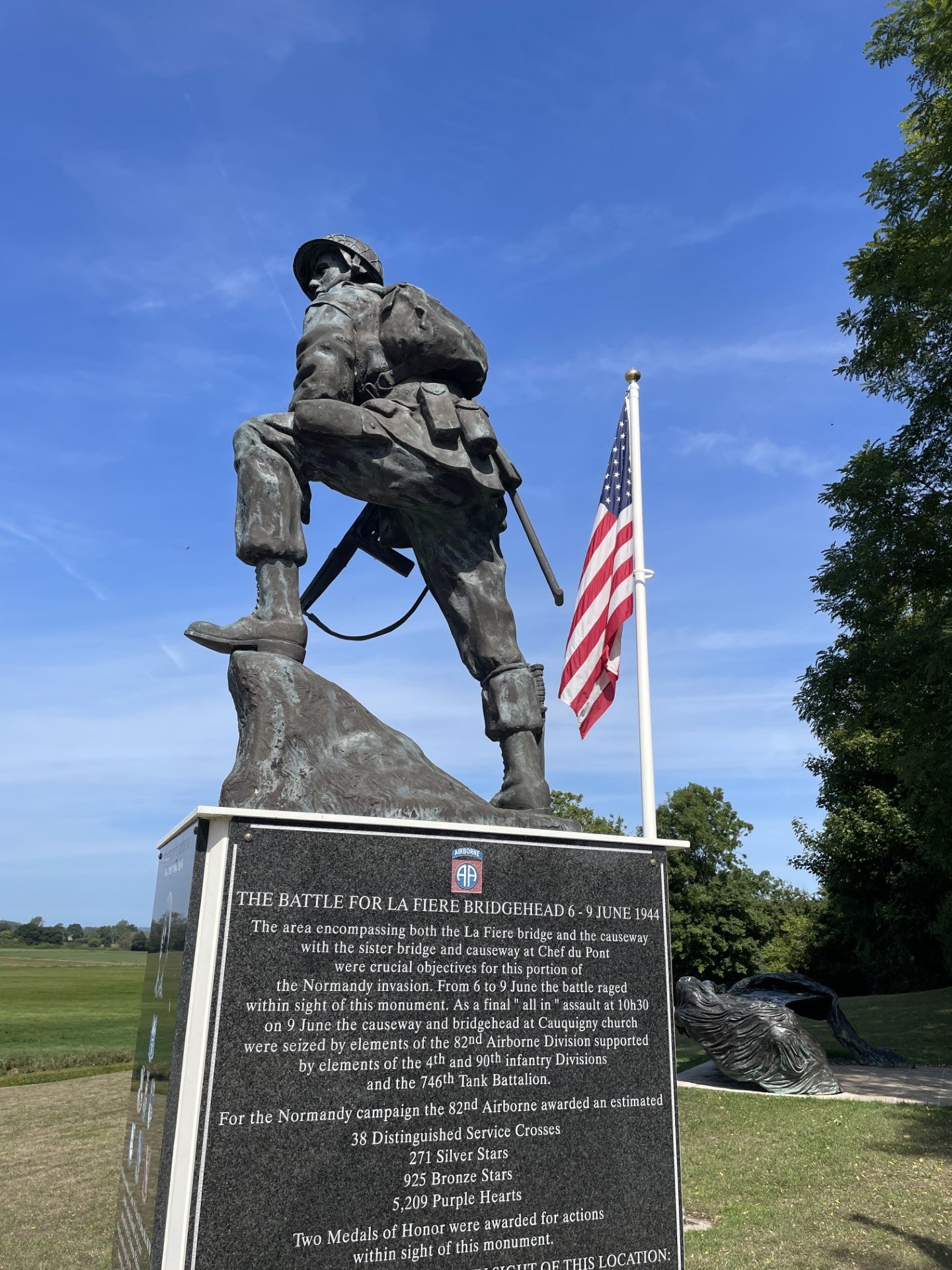 Iron Mike. Statue of a soldier with a plaque and American flag in the background near La Fiere Bridge.